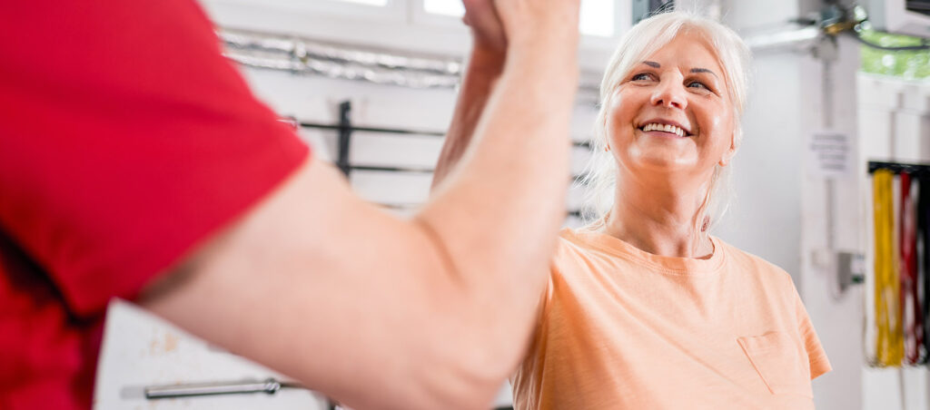 Older lady taking weight loss drugs like Ozempic giving personal trainer in gym a high five as part of GLP-1 weight loss journey