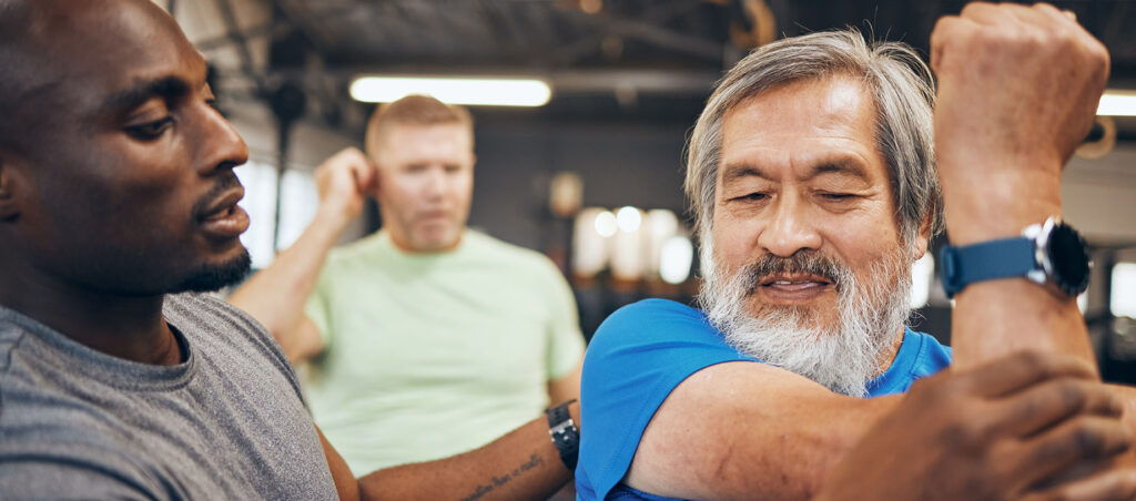 Older man exercises in a gym with personal trainer for strength, flexibility, and cardio function while on a GLP-1 medical weight loss journey