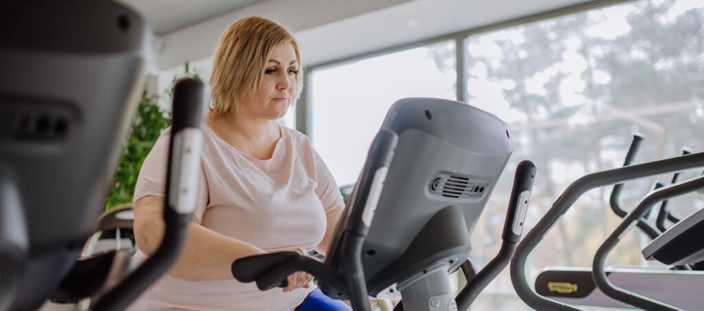 Overweight lady exercising on an elliptical machine at the gym to lose weight while taking GLP-1 medications for weight loss and diabetes management