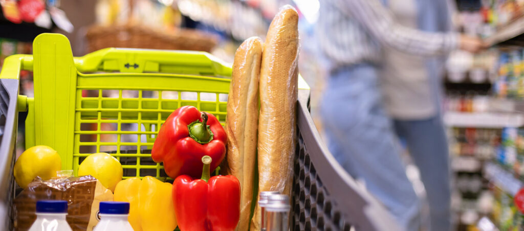 View of grocery cart full of colorful vegetables, protein, fruits, and complex carbs while lady shops for her GLP-1 weight loss meal plan