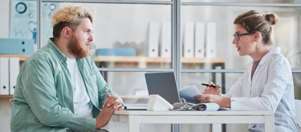 Young man talking to medical weight loss doctor in office while considering a GLP-1 prescription like Ozempic (Semaglutide) to improve health