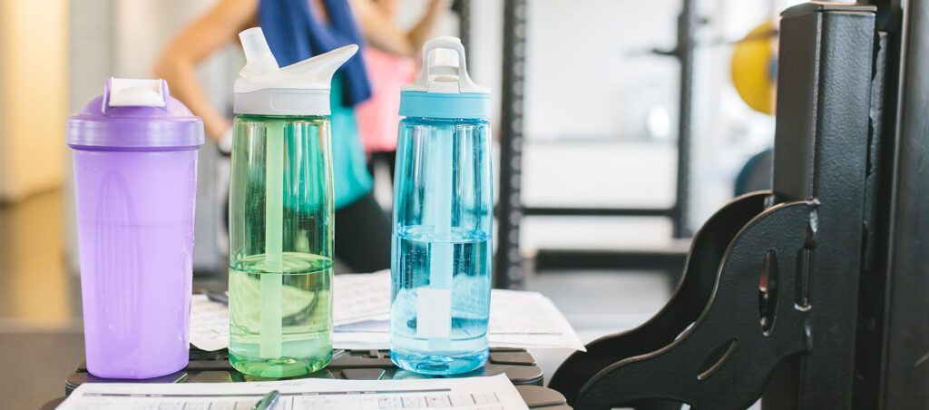 Water bottles and clipboard with exercise schedule in a gym setting as a GLP-1 patient exercises to lose weight while taking prescription Zepbound, Trulicity, or Saxenda