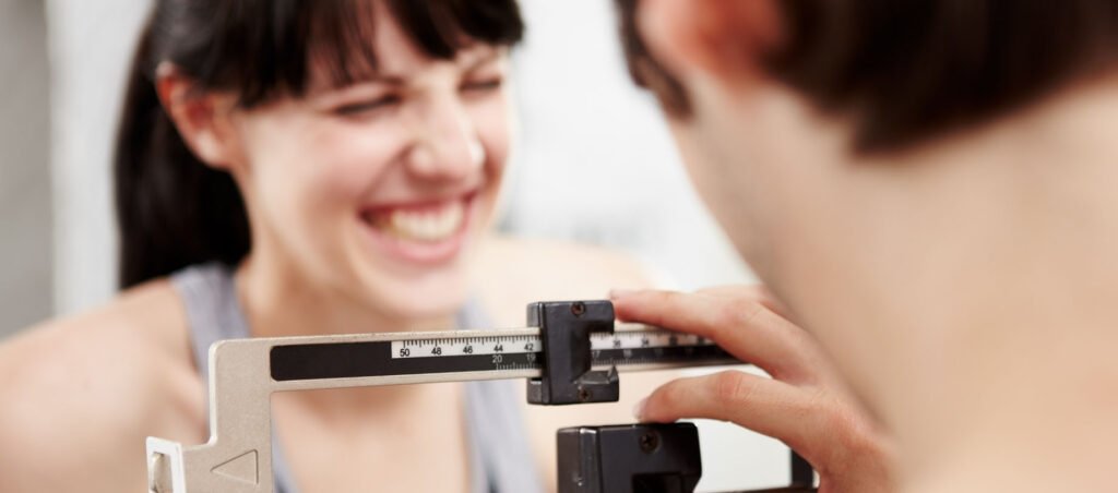 Lady weighs herself in medical office and smiles with weight loss progress while taking prescription Semaglutide (Ozempic, Rybelsus, Wegovy)