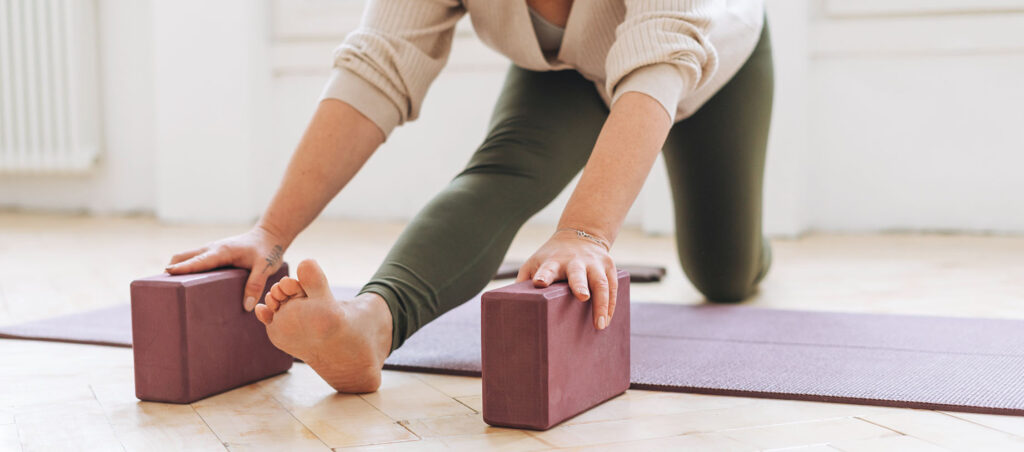 Lady stretches with yoga blocks at home for general exercise and wellness to support a holistic medical weight loss journey with a GLP-1 prescription