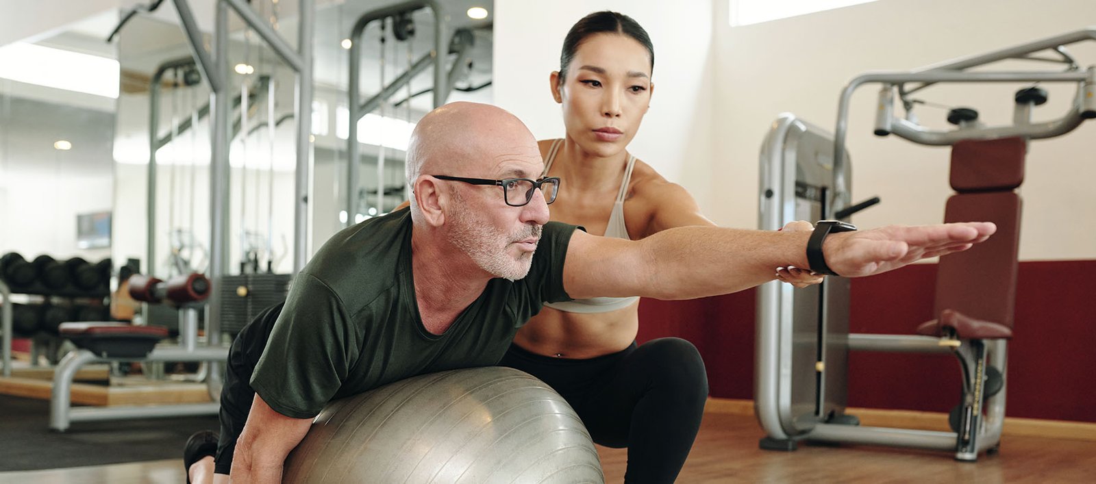 Older man working with a personal trainer at a country club gym to promote flexibility, balance, and overall wellness.