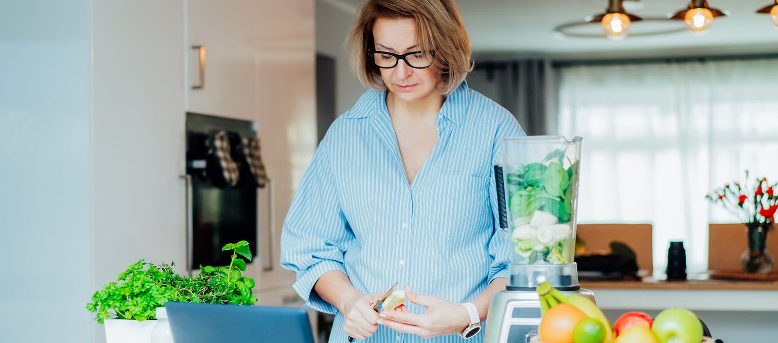Older lady making healthy smoothie with fruits and vegetables in kitchen to prioritize better nutrition.