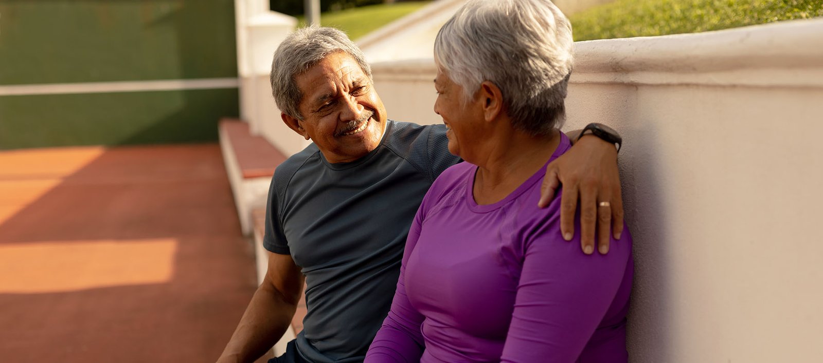 Diverse happy older couple sitting on a bench at a country club or wellness club after a tennis match for exercise and longevity.