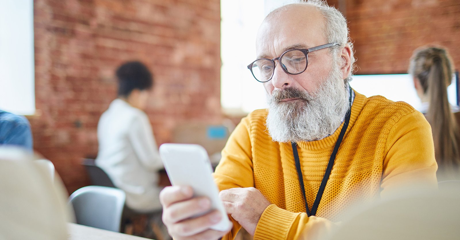 Older employee in a modern office checking a mobile wellness app, illustrating the future of workplace wellness.